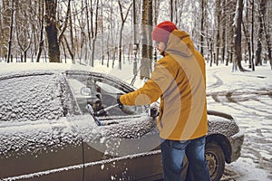 Man cleaning snow from car windshield with brush