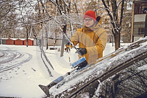 Man cleaning snow from car windshield with brush