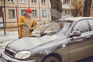 Man cleaning snow from car windshield with brush