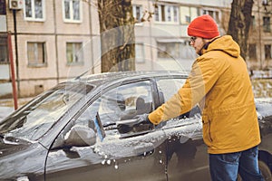Man cleaning snow from car windshield with brush