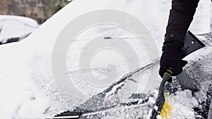 A man cleaning snow from car windshield outdoors on winter day