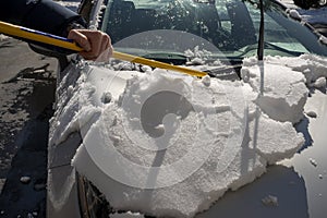 man cleaning snow off his car using ice scrapper after winter snowfall.