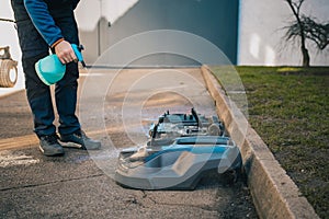 Man cleaning the underside of a robotic autonomous lawnmower with the help of a cleaning solvent as part of a service plan. Gunk