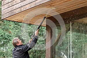 Man cleaning walls and floor with high pressure power washer. Washing terrace wood planks and cladding walls.