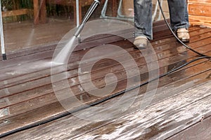 Man cleaning walls and floor with high pressure power washer. Washing terrace wood planks and cladding walls.