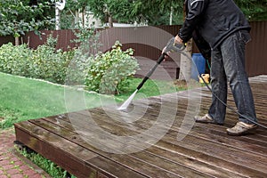 Man cleaning walls and floor with high pressure power washer. Washing terrace wood planks and cladding walls.