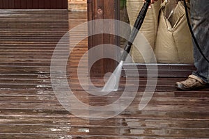 Man cleaning walls and floor with high pressure power washer. Washing terrace wood planks and cladding walls.