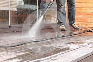 Man cleaning walls and floor with high pressure power washer. Washing terrace wood planks and cladding walls.