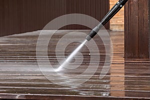 Man cleaning walls and floor with high pressure power washer. Washing terrace wood planks and cladding walls.