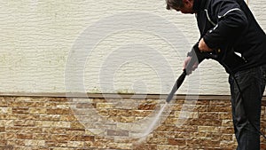 Man cleaning walls with high pressure power washer. Washing cladding walls house.