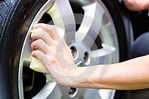 Man cleaning wheel rim while car wash
