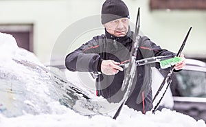 Man cleaning wipers on a frosty winter day before starting the drive