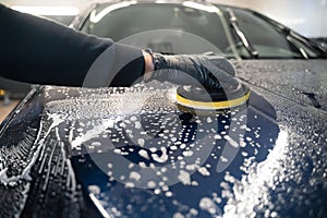 Man cleans car hood with circle sponge. Preparing auto for polishing. .Detailed car wash