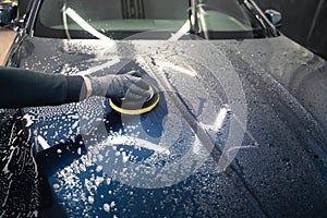 Man cleans car hood with circle sponge. Preparing auto for polishing. .Detailed car wash.
