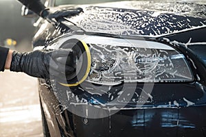 Man cleans car lamp with circle sponge. Preparing auto for polishing. .Detailed car wash.