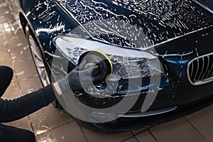 Man cleans car lamp with circle sponge. Preparing auto for polishing. .Detailed car wash.