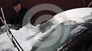 A man cleans a car windshield from snow with a brush. Winter in Russia, the car was covered with snow