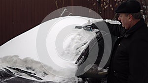 A man cleans a car windshield from snow with a brush. Winter in Russia, the car was covered with snow