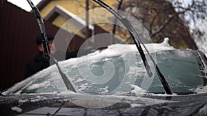 A man cleans a car windshield from snow with a brush. Winter in Russia, the car was covered with snow