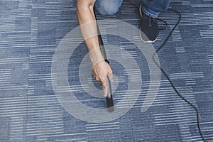 A man cleans the carpet flooring of an office with an upright vacuum cleaner with an attached extension wand