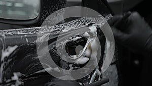 A man cleans the interior of a car with foam and a brush. Clean the door trim.