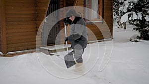 Man Cleans A Shovel Yard From Snow On The Background Of A Wooden House In Winter