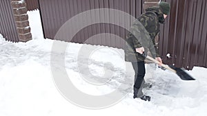 Man cleans the snow with a big shovel near the house