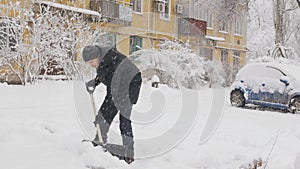 A man cleans snow with a big shovel in the yard.