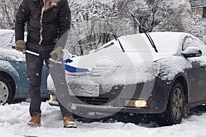 Man cleans snow from a car on a winter morning