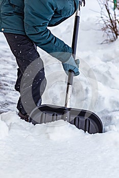 A man cleans the snow near the house with a big black shovel.