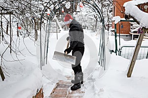 A man cleans steps from snow. In a red hat of Santa Claus and a leather black jacket. In felt boots. Clearing snow from the backya