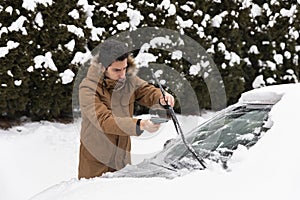 A man cleans the wipers of the car from the snow and ice that fell at night