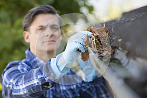 Man Clearing Leaves From Guttering Of House