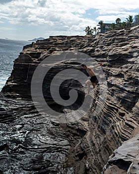 Man cliff jumping off Spitting Cave on Oahu, Hawaii
