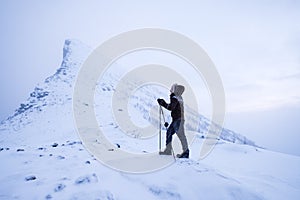 Man climber with trekking poles standing on snowy mountain peak