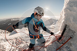 man with climbing equipment fixes rope on mountain slope against the backdrop of landscape and sky photo