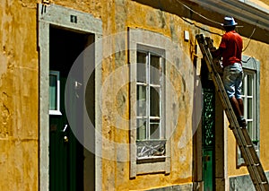 A man climbing a ladder seems to be painting a wall and checking some wire