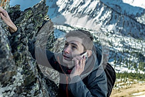 Man climbing the mountain to the top and talking on the phone. Communications and goal achievement in career