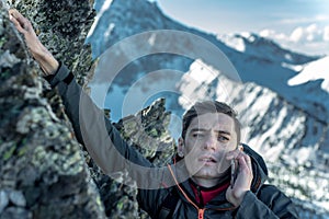 Man climbing the mountain to the top and talking on the phone. Communications and goal achievement in career