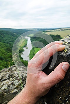 Man climbing on rock outdoor, close-up image of climber hand with river and nature in background