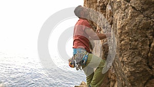 A man is climbing a rock wall while wearing a red shirt