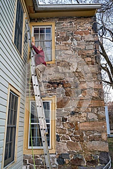 Man climbs a ladder leaning against a historic old stone home