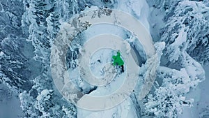 The man climbs on mountain peak and rejoice at success. Wild snowy forest around