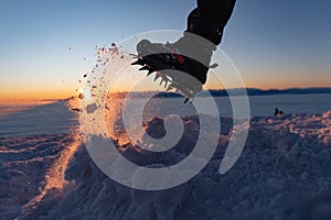 Man climbs a mountain peak in winter during sunrise. A shoe with spikes on - crampons.