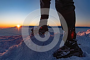 Man climbs a mountain peak in winter during sunrise. A shoe with spikes on - crampons.