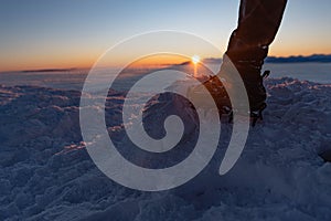 Man climbs a mountain peak in winter during sunrise. A shoe with spikes on - crampons.