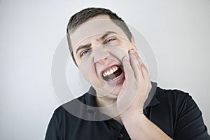 A man clings to his cheek and winces in pain in his tooth. The concept of dental problems, caries, tooth decay, flux. White