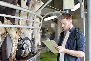 Man with clipboard and milking cows on dairy farm