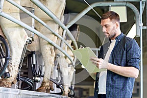 Man with clipboard and milking cows on dairy farm