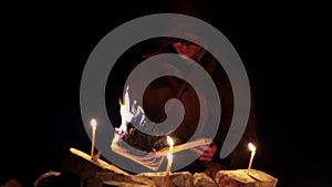 a man in a cloak with a hood is reading a hot book with candles on the floor